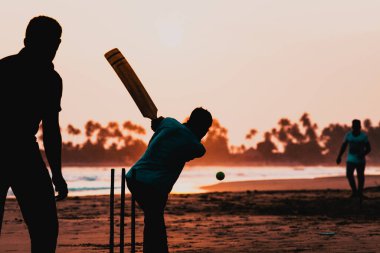 silhouette of boys playing cricket by the sea