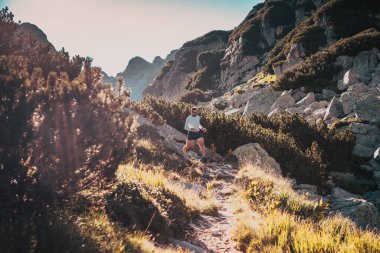 Gün batımında dağ manzarasında koşan patika koşucusu aktif yaşam tarzı