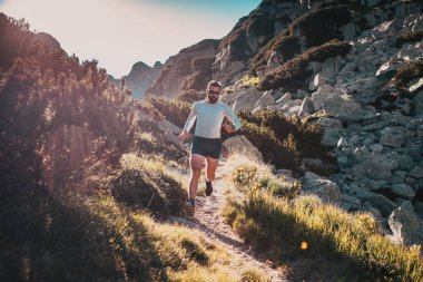 Gün batımında dağ manzarasında koşan patika koşucusu aktif yaşam tarzı