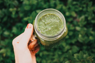 Kadının elinde yeşil soğuk sıkılmış meyve suyu dolu bir kavanoz var. Sağlıklı beslenme, detoks, meyve suyu, vücut temizleme konsepti