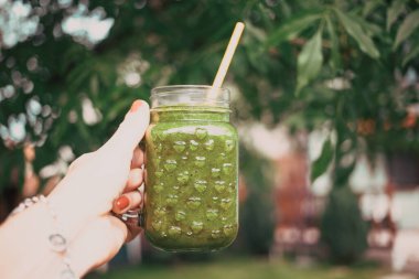 Kadının elinde yeşil soğuk sıkılmış meyve suyu dolu bir kavanoz var. Sağlıklı beslenme, detoks, meyve suyu, vücut temizleme konsepti