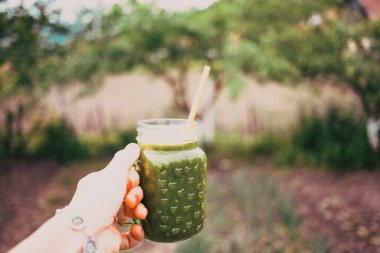 Kadının elinde yeşil soğuk sıkılmış meyve suyu dolu bir kavanoz var. Sağlıklı beslenme, detoks, meyve suyu, vücut temizleme konsepti
