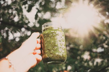 Kadının elinde yeşil soğuk sıkılmış meyve suyu şişesi var. Sağlıklı beslenme, detoks, meyve suyu, vücut temizleme konsepti