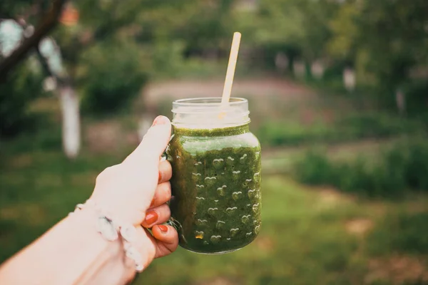 女人的手拿着一个装有绿色冷榨果汁的罐子 自然背景 健康饮食 身体清洁概念 — 图库照片