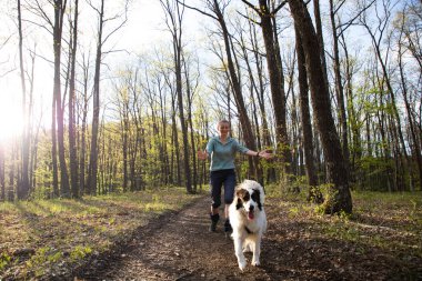 Bir kadın köpekle ormanda yürüyor.