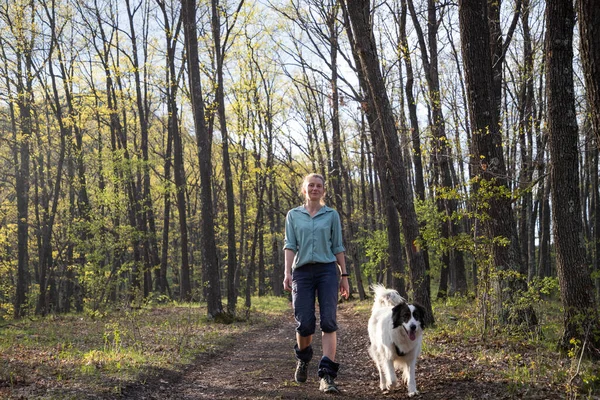 Bir kadın köpekle ormanda yürüyor.