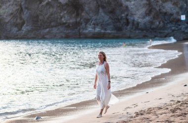 Beyazlı kadın kumsalda yürüyor.