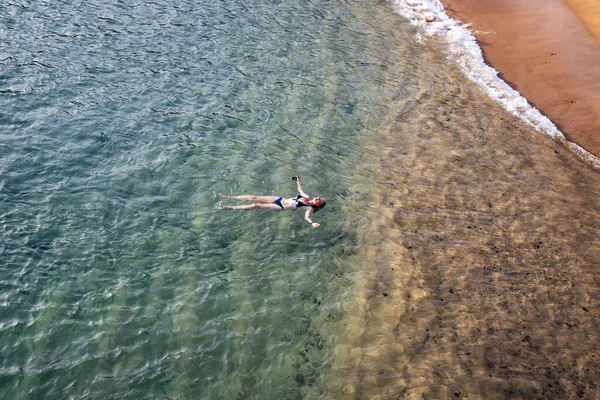 top view of woman floating in the sea near sandy beach