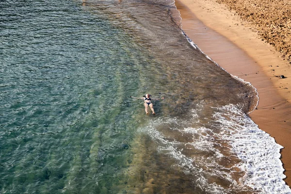 top view of woman floating in the sea near sandy beach