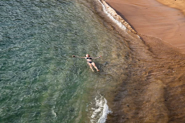 top view of woman floating in the sea near sandy beach