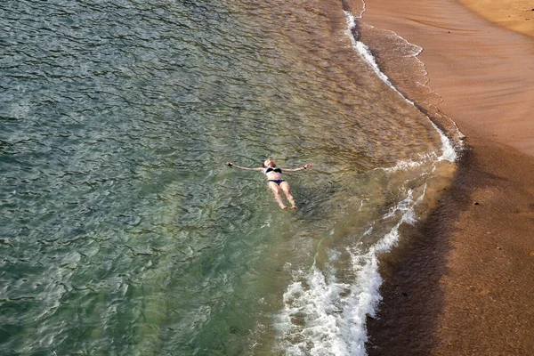 top view of woman floating in the sea near sandy beach