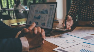 Kafesinde çalışan ve dizüstü bilgisayar kullanan genç iş adamlarının başarılı takım çalışmalarının sonuçlarını gösteren çizelge ve grafikleri ellerinde tuttukları düşünülürse....