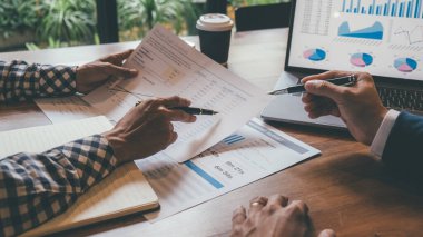 Kafesinde çalışan ve dizüstü bilgisayar kullanan genç iş adamlarının başarılı takım çalışmalarının sonuçlarını gösteren çizelge ve grafikleri ellerinde tuttukları düşünülürse....