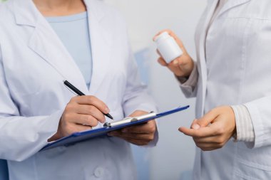 Eczanedeki panoya yazı yazan beyaz önlüklü bir eczacının elinde şişe vardı. 