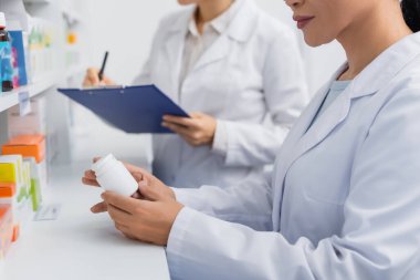 Beyaz önlüklü eczacının, bulanık meslektaşının yanında eczanede panoya yazı yazarken kısmi görüntüsü 