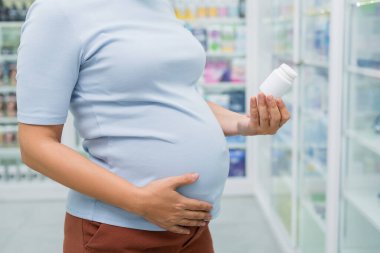 Eczanede vitaminli bir şişe taşıyan hamile müşterinin kırpılmış görüntüsü.
