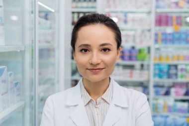 brunette pharmacist smiling while looking at camera  clipart