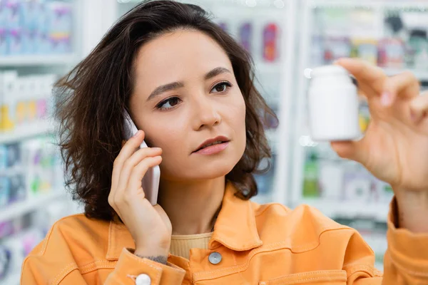 Esmer Kadın Eczanede Akıllı Telefonla Konuşurken Elinde Ilaç Şişesi Tutuyor — Stok fotoğraf