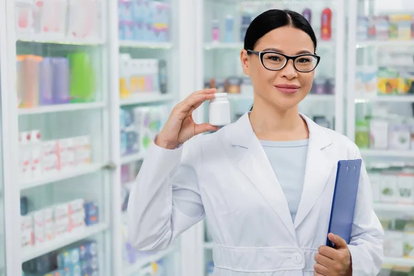 Ázsiai Gyógyszerész Szemüvegben Mosolyog Miközben Tartja Üveg Gyógyszeres Írótábla — Stock Fotó
