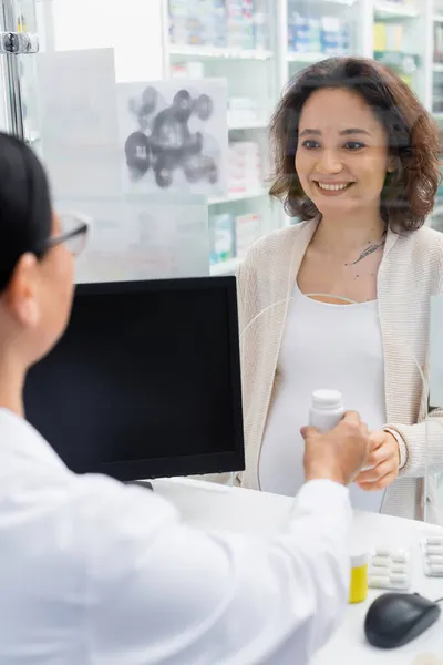 Vrolijke Zwangere Vrouw Zoek Naar Wazig Aziatische Apotheker Buurt Van — Stockfoto