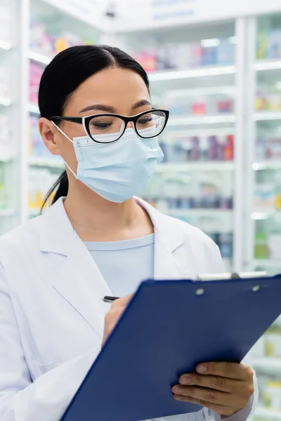 Asian Pharmacist Glasses Medical Mask Holding Blurred Clipboard — Stock Photo, Image