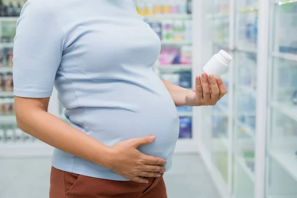 孕妇在药店里拿着装有维生素的瓶子的景象 — 图库照片