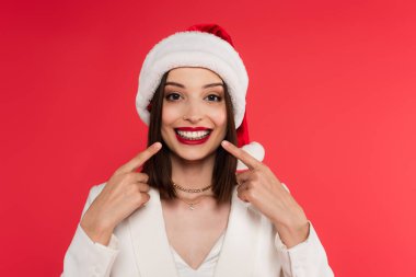 Noel Baba şapkalı gülümseyen kadın kırmızı dişlere bakıyor. 