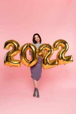 2022 numaralı pembe arka planda balonların yanında gülümseyen şık bir kadın.