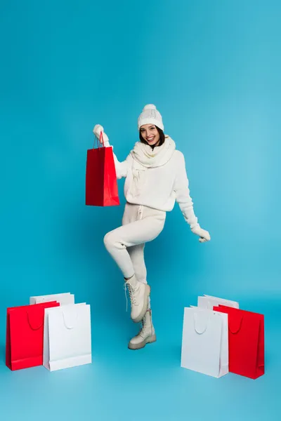 Sıcak Şapkalı Eldivenli Olumlu Bir Kadın Mavi Arka Planda Alışveriş — Stok fotoğraf
