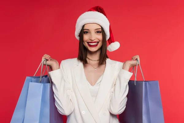 戴着圣诞礼帽 穿着白色夹克 提着红色购物袋的快乐女人 — 图库照片