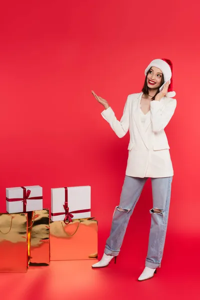 Lächelnde Frau Mit Weihnachtsmütze Spricht Auf Smartphone Neben Geschenken Und — Stockfoto