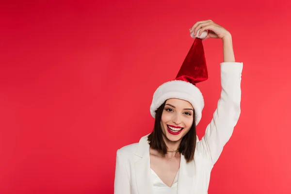 Beyaz Ceketli Elinde Noel Baba Şapkası Tutan Gülümseyen Kadın Kırmızıda — Stok fotoğraf