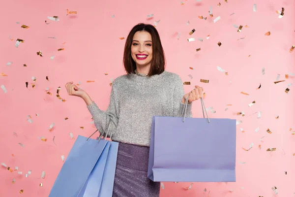 Stijlvolle Vrouw Trui Houden Boodschappentassen Onder Confetti Roze Achtergrond — Stockfoto