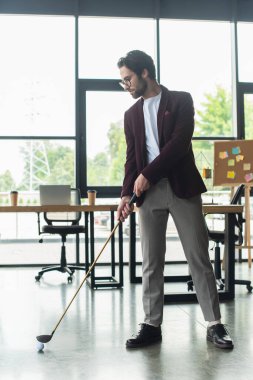 Ofiste golf oynayan gözlüklü genç işadamının yan görüntüsü 