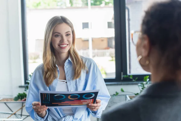 Glimlachende Zakenvrouw Met Document Buurt Wazig Afrikaans Amerikaanse Collega Functie — Stockfoto