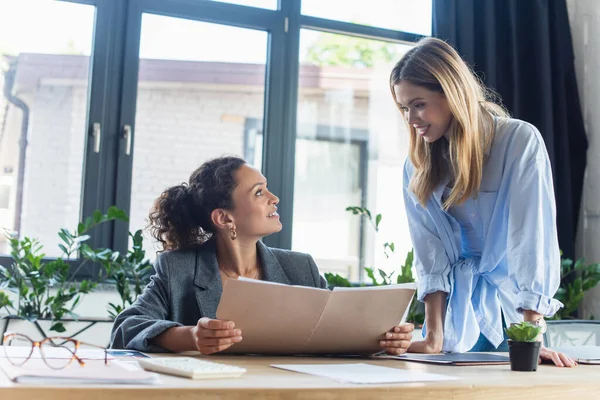 Positive Geschäftsfrau Blickt Auf Afrikanisch Amerikanische Kollegin Mit Papiermappe Büro — Stockfoto