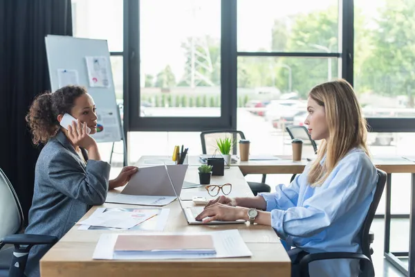 Empresaria Afroamericana Hablando Smartphone Mirando Colega Con Laptop Oficina — Foto de Stock