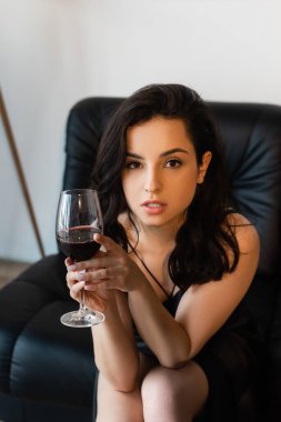 Baştan çıkarıcı kadın iç çamaşırlı, elinde şarap bardağıyla kanepede oturuyor.