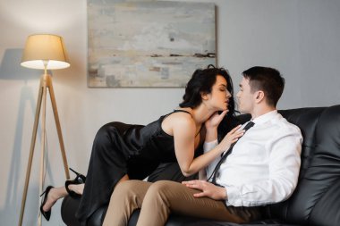 Kanepede erkek arkadaşını baştan çıkaran siyah iç çamaşırlı seksi genç kadının yan görüntüsü. 