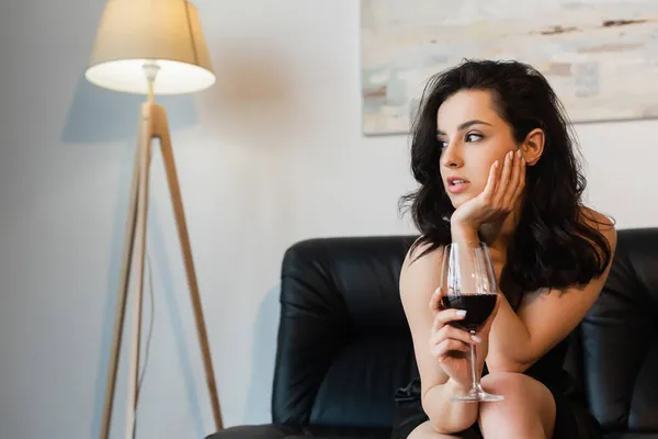 pretty woman in black slip dress holding glass of wine and sitting on sofa