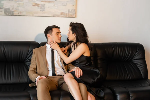 brunette woman in black slip dress seducing man on sofa