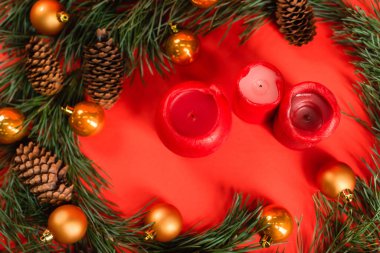 Yeşil dalların yakınındaki çam kozalaklarının en üst görüntüsü Noel baloları ve kırmızıda mumlar