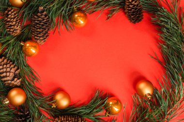 Yeşil dalların yakınındaki çam kozalaklarının kırmızı üzerinde noel topları