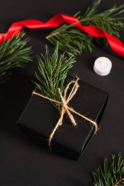 top view of gift box with fir branch near candle and blurred red ribbon on black clipart