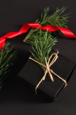 top view of gift box with fir branch near blurred red ribbon on black clipart