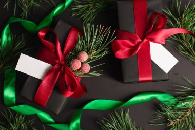 top view of wrapped gift boxes with blank cards near blurred fir branches on black  clipart