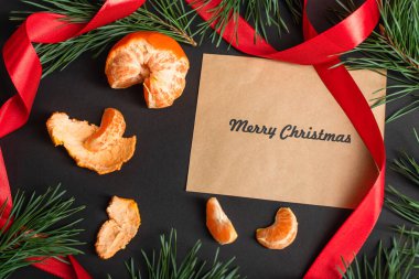 Zanaat kağıdının en üst görüntüsünde soyulmuş mandallar ve siyah üzerine köknar dalları olan mutlu noel mektupları var.