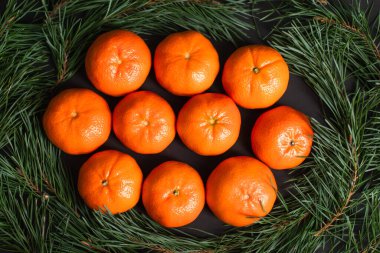 Köknar dallarının yanındaki altın noel toplarının yanındaki olgun mandalinaların en üst görüntüsü.