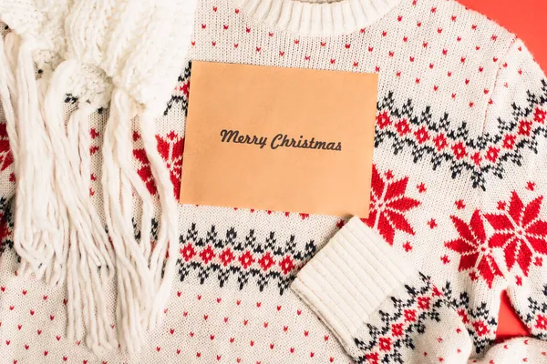 スカーフの近くのニットセーターにメリークリスマスのレタリング付きグリーティングカードのトップビュー — ストック写真