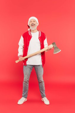Gülümseyen orta yaşlı, Noel Baba şapkalı, elinde baltayla kırmızı bir adam.